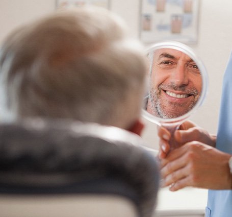 Man smiling at reflection in handheld mirror