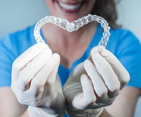 dental team member holding two aligners in the shape of a heart 