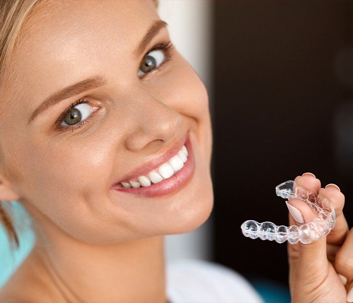 Smiling woman holding Invisalign clear aligner tray