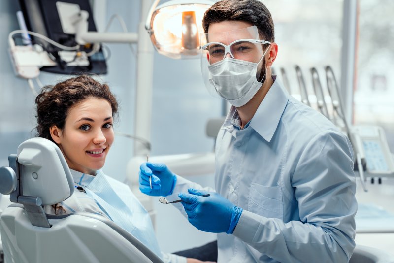 a dentist wearing PPE while preparing to assist a female patient in need of dental care