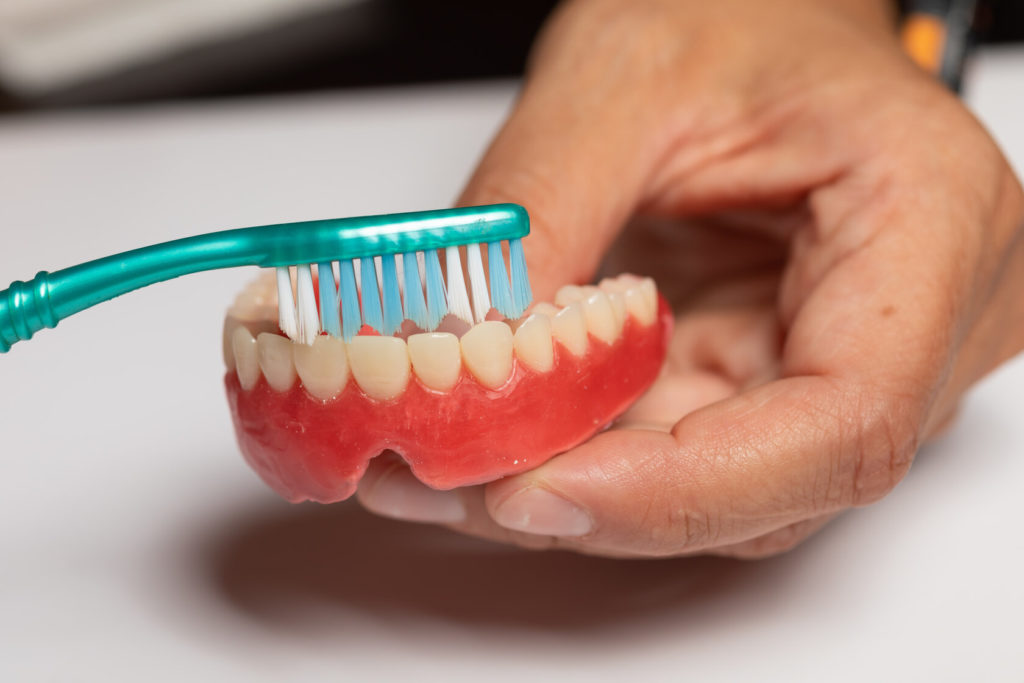 patient cleaning dentures in Spring with a toothbrush