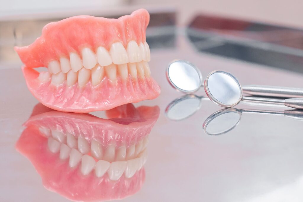 Complete set of dentures next to dental mirrors on reflective surface